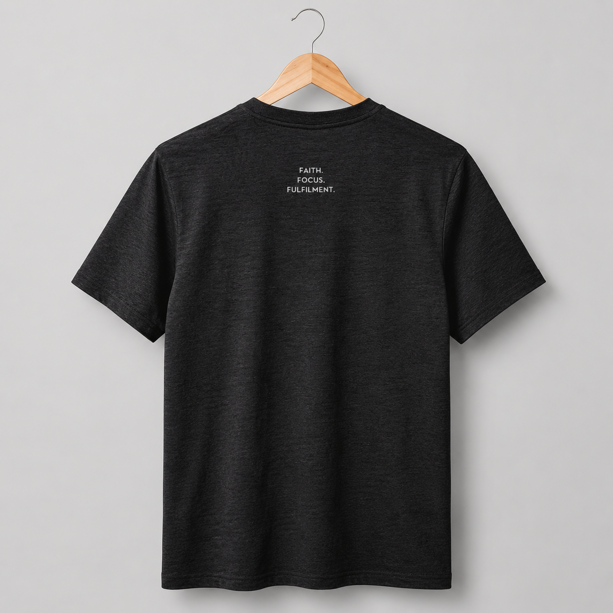 A black short-sleeve crewneck t-shirt hanging on a wooden hanger. The back of the shirt features a small slogan Faith. Focus. Fulfilment. in white text between the shoulder blades.