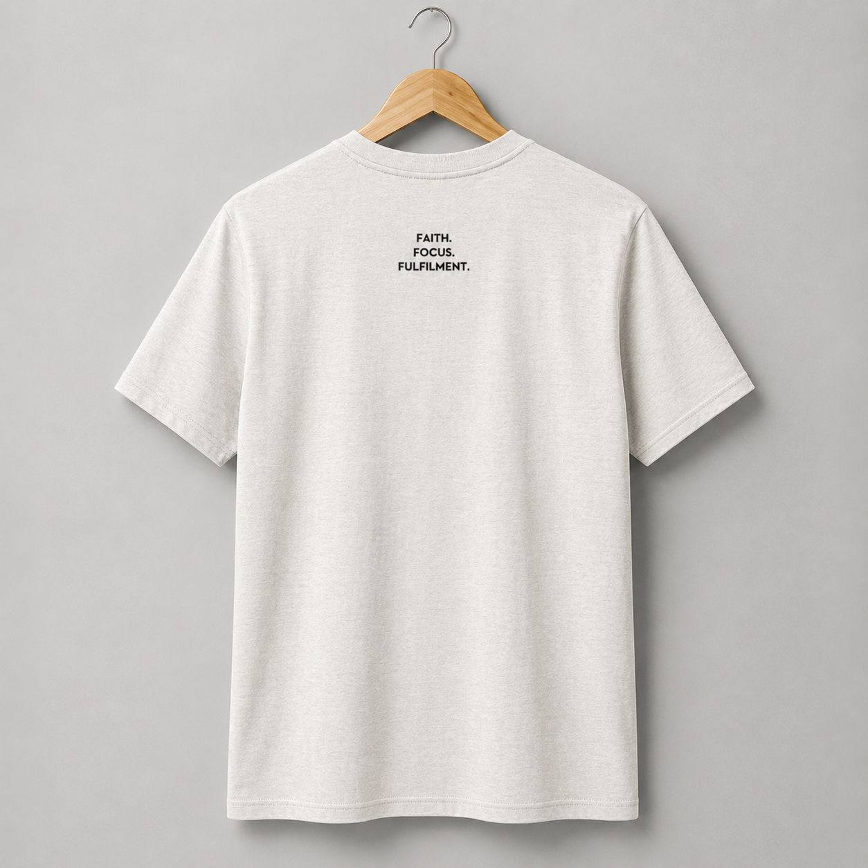 A vintage white short-sleeve crewneck t-shirt hanging on a wooden hanger. The back of the shirt features a small slogan Faith. Focus. Fulfilment. in black text between the shoulder blades.