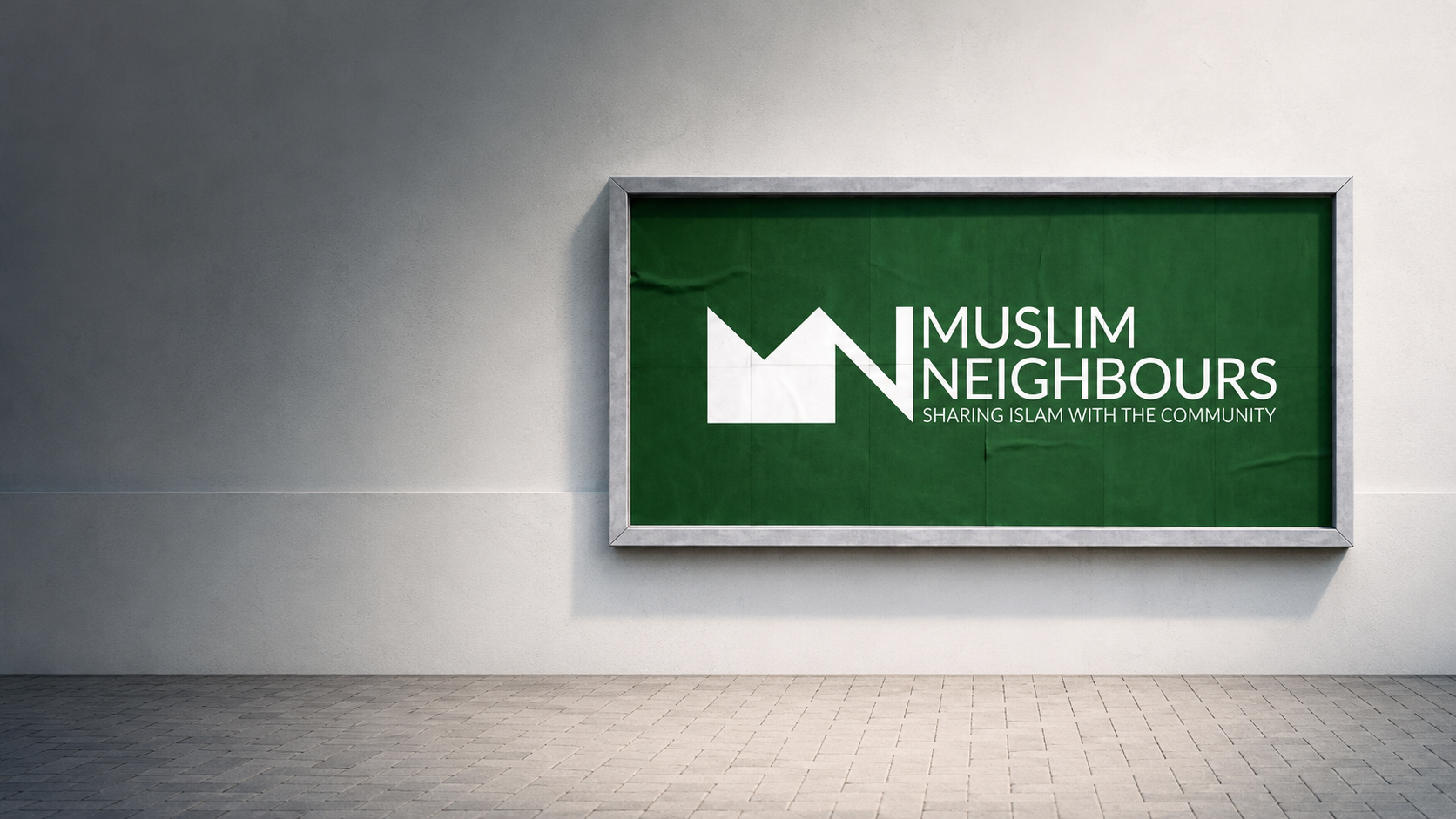 A framed green sign with the Muslim Neighbours logo and text, mounted on a light gray wall above a tiled floor.