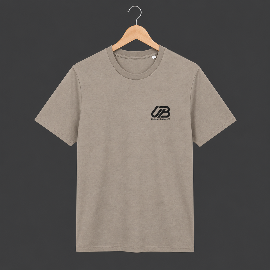 A dessert dust coloured short-sleeve crewneck t-shirt hanging on a wooden hanger. The shirt features a small black 'UB' logo on the left chest with 'Ummah Balance' printed underneath.