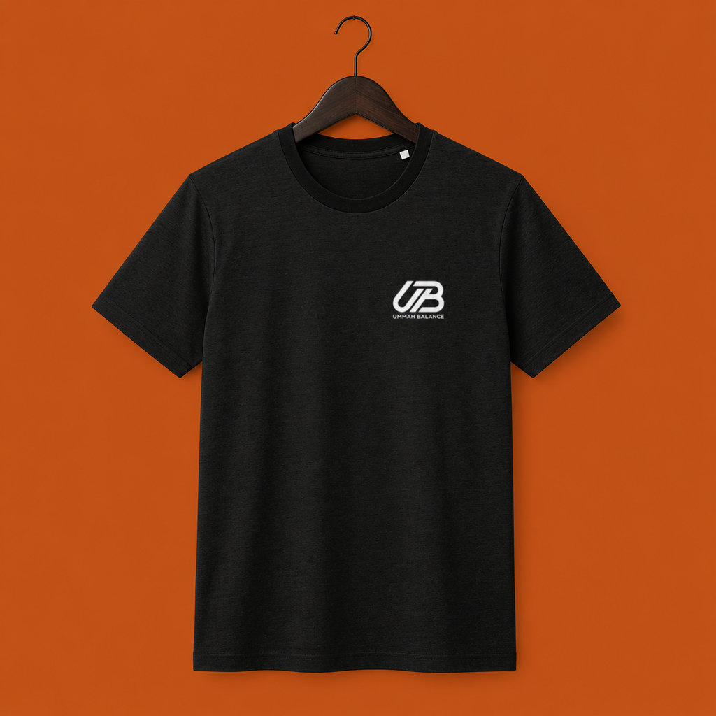 A black short-sleeve crewneck t-shirt hanging on a dark wooden hanger. The shirt features a small white 'UB' logo on the left chest with 'Ummah Balance' printed underneath.
