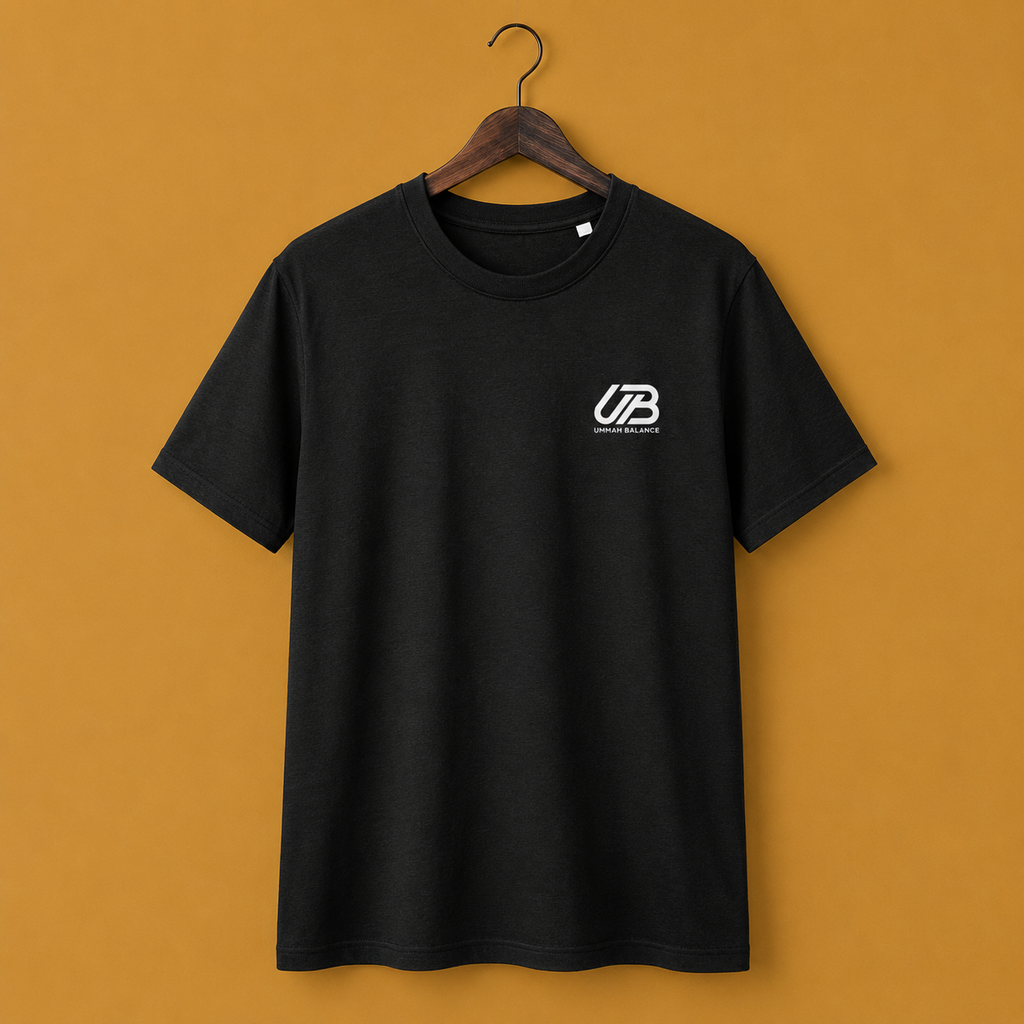 A black short-sleeve crewneck t-shirt hanging on a wooden hanger. The shirt features a small white 'UB' logo on the left chest with 'Ummah Balance' printed underneath.