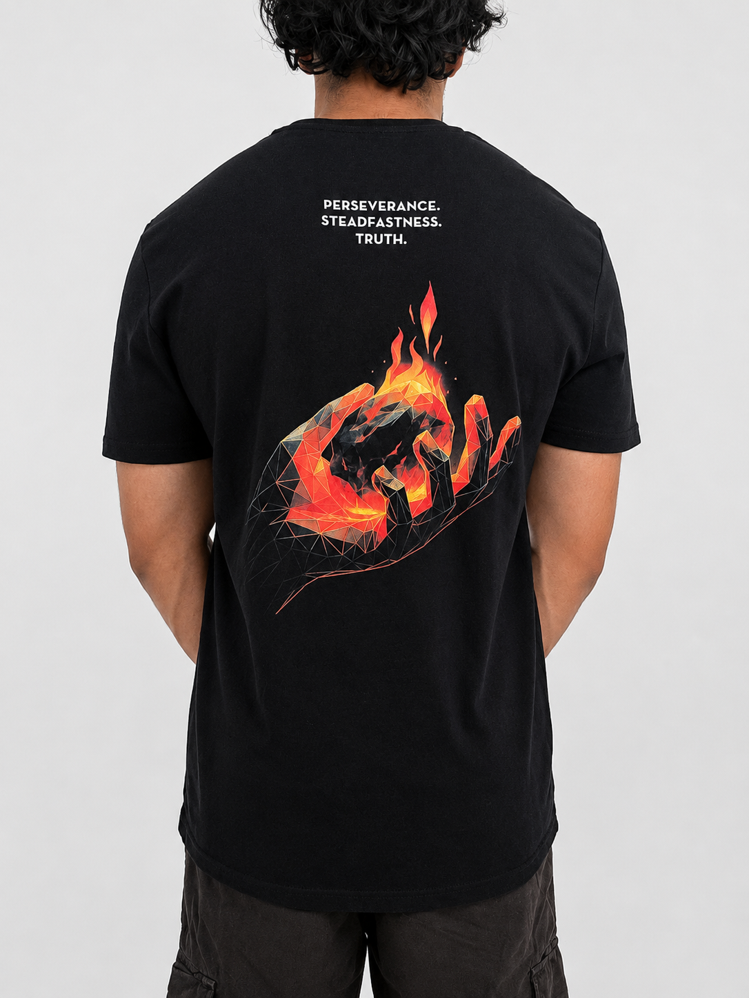 A man viewed from behind wearing a black t-shirt with a graphic of a hand holding a burning ember, with the words 'PERSEVERANCE. STEADFASTNESS. TRUTH'