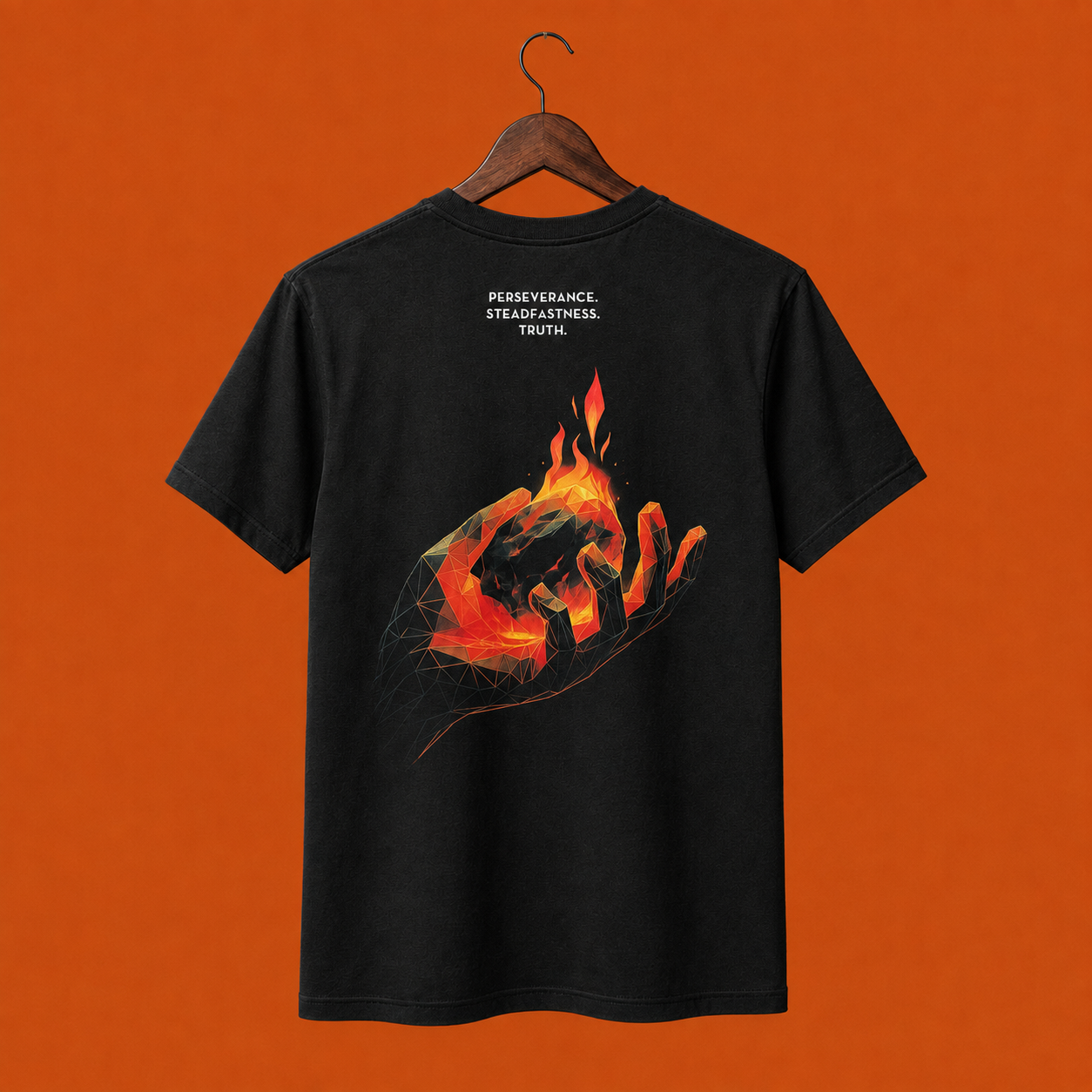 A black short-sleeve t-shirt hanging on a wooden hanger. The back of the shirt features a graphic print of a geometric styled hand holding a burning ember with the words Perseverance, Steadfastness and Truth white text above the graphic.